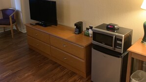 Een kleine hotelkamer met een houten dressoir, een televisie, een magnetron, een kleine koelkast, een prullenbak en een stoel.