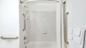 Een badkamer met een inloopdouche, handgrepen en een witte betegelde wand.