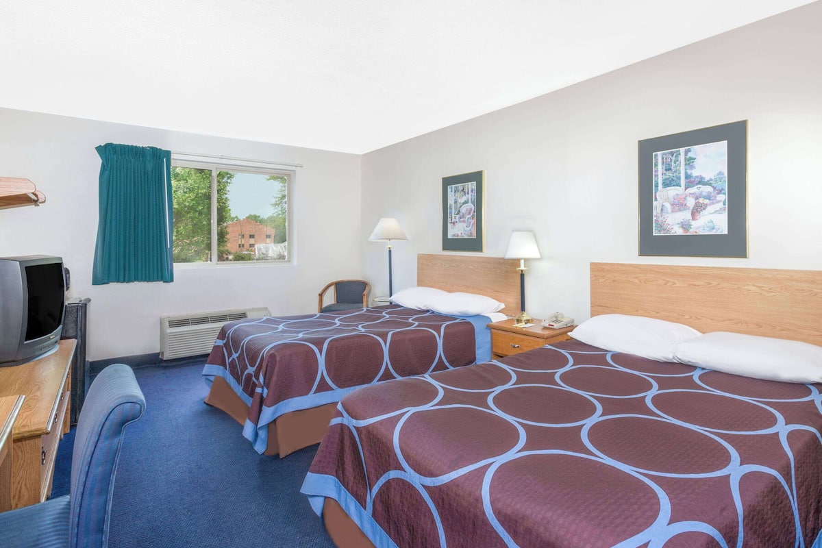 A hotel room with two beds, a desk with a television, a chair, and two bedside lamps.