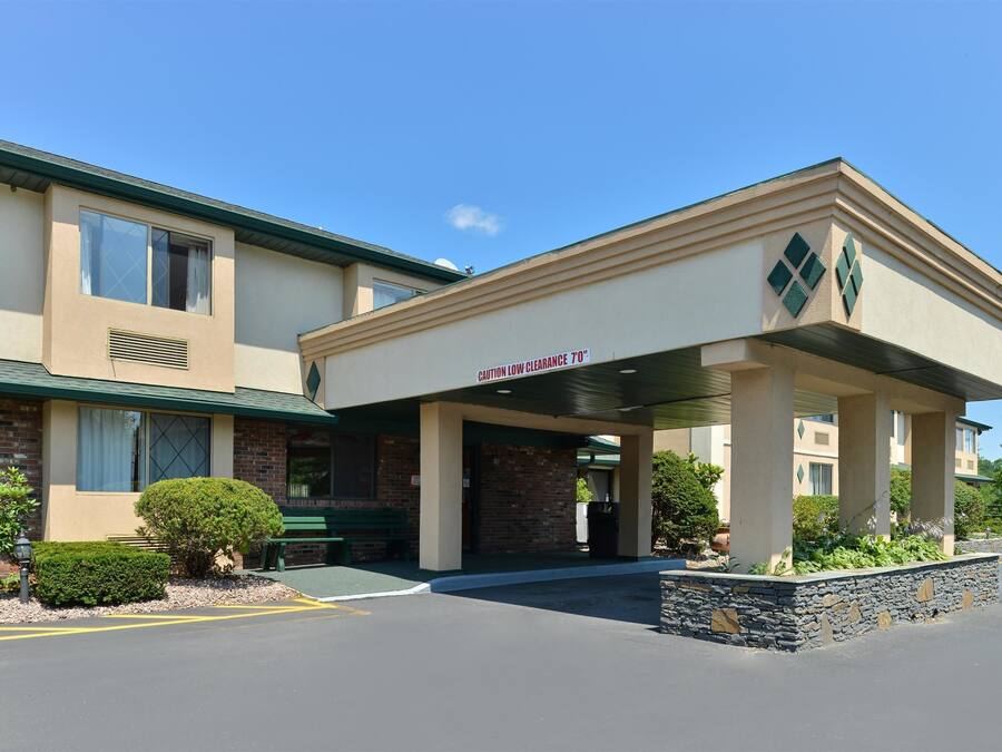 A hotel entrance with a covered walkway, a sign indicating low clearance, and a flag.