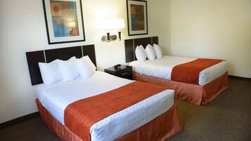 Habitación de hotel con dos camas, cada una con ropa blanca y falda marrón. Dos lámparas fijadas a la pared y dos cuadros enmarcados encima de las camas.