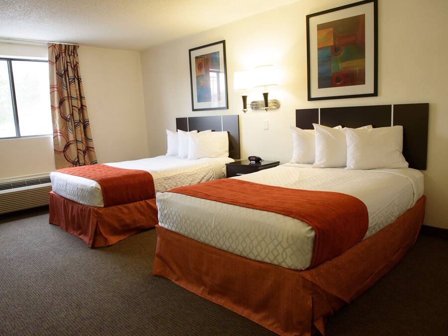 A hotel room with two beds, a heater, a window with curtains, and artwork on the walls.
