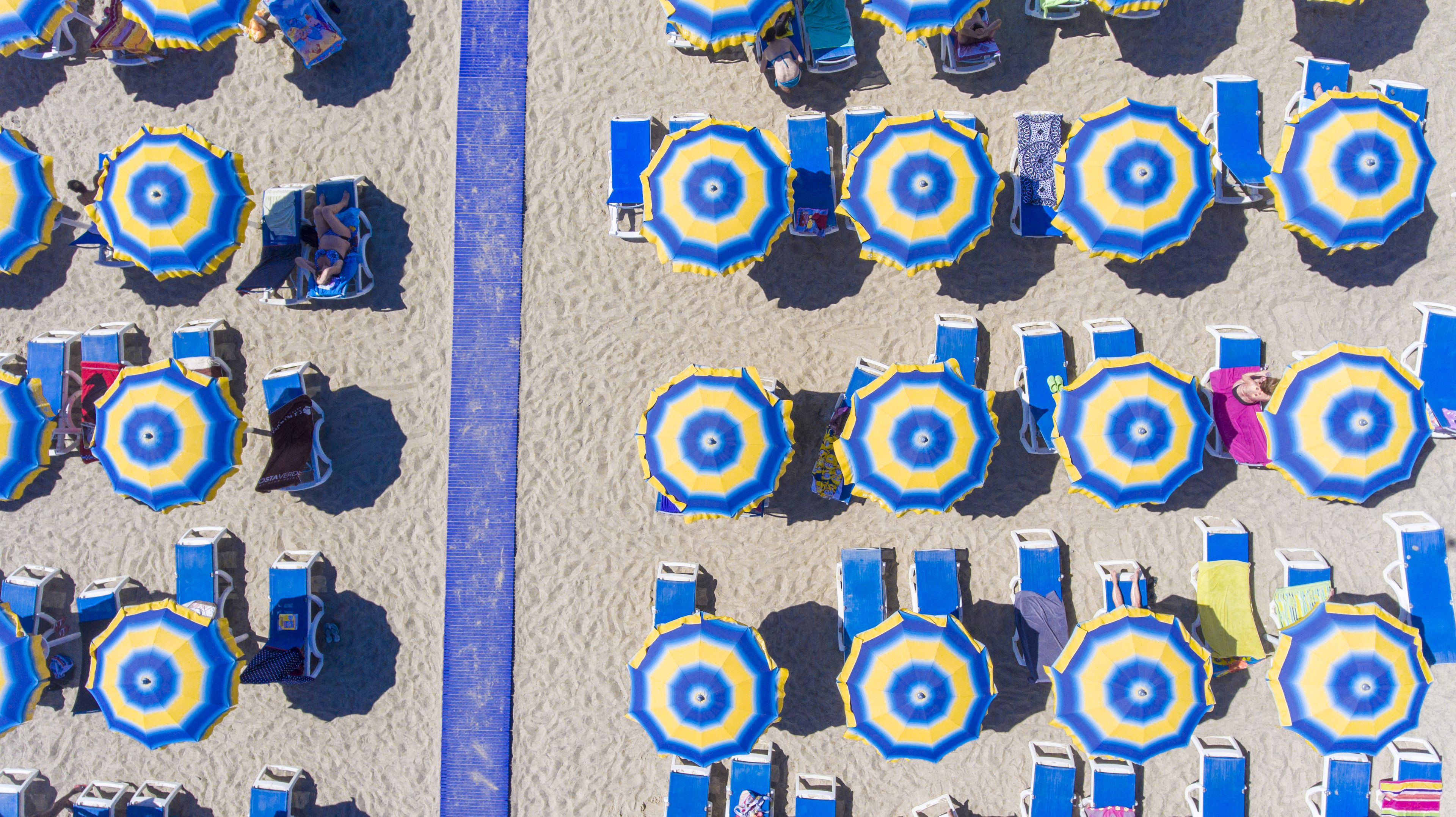 Une plage bordée de rangées de parasols bleus et jaunes et de chaises de plage.