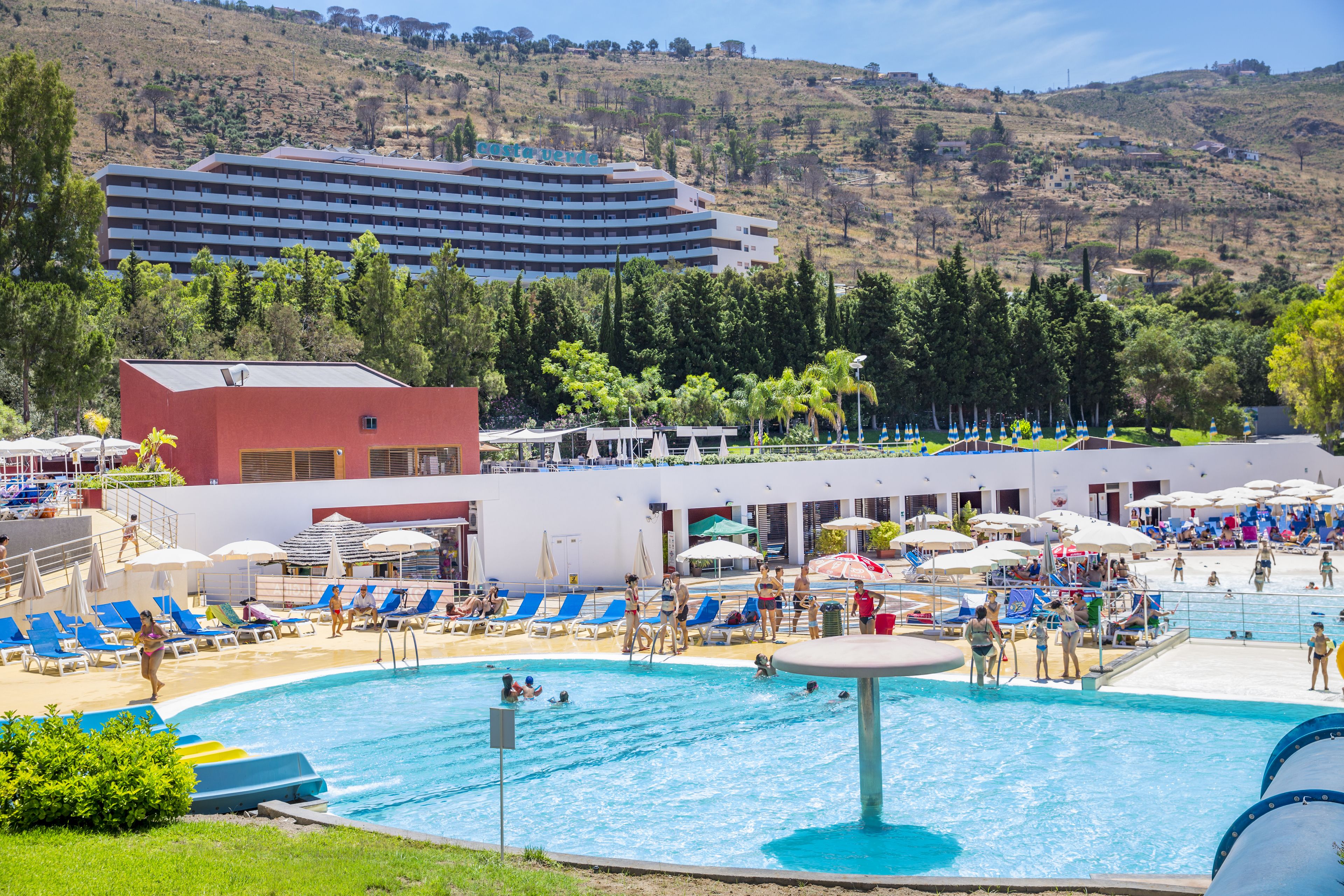 Un hotel con piscina, lettini e vista su un paesaggio collinare.