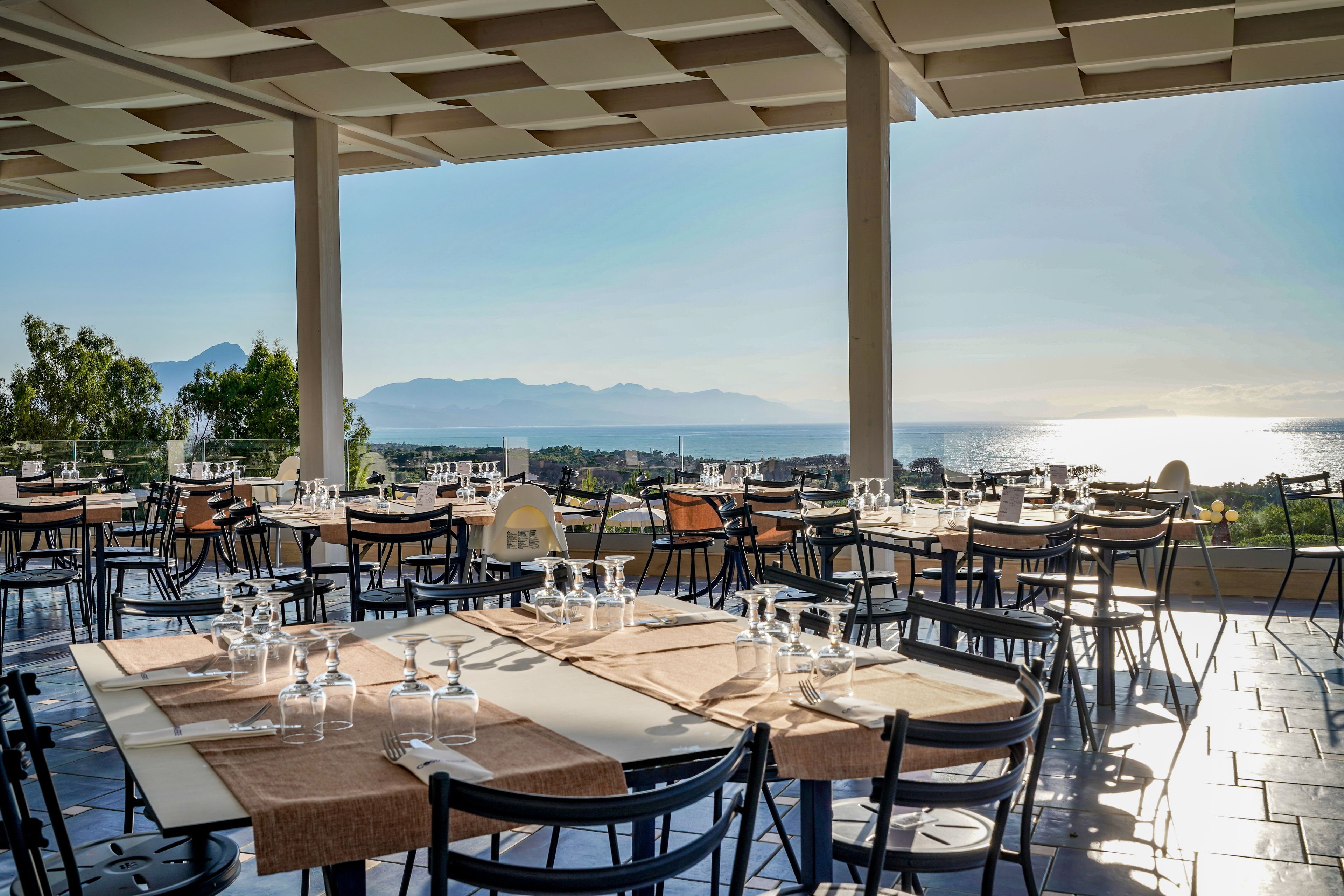 Zona pranzo all'aperto con tavoli apparecchiati per gli ospiti, con vista panoramica sul mare e sulle montagne.