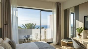 A modern hotel room with a large balcony, a bed, a desk, and a chair.
