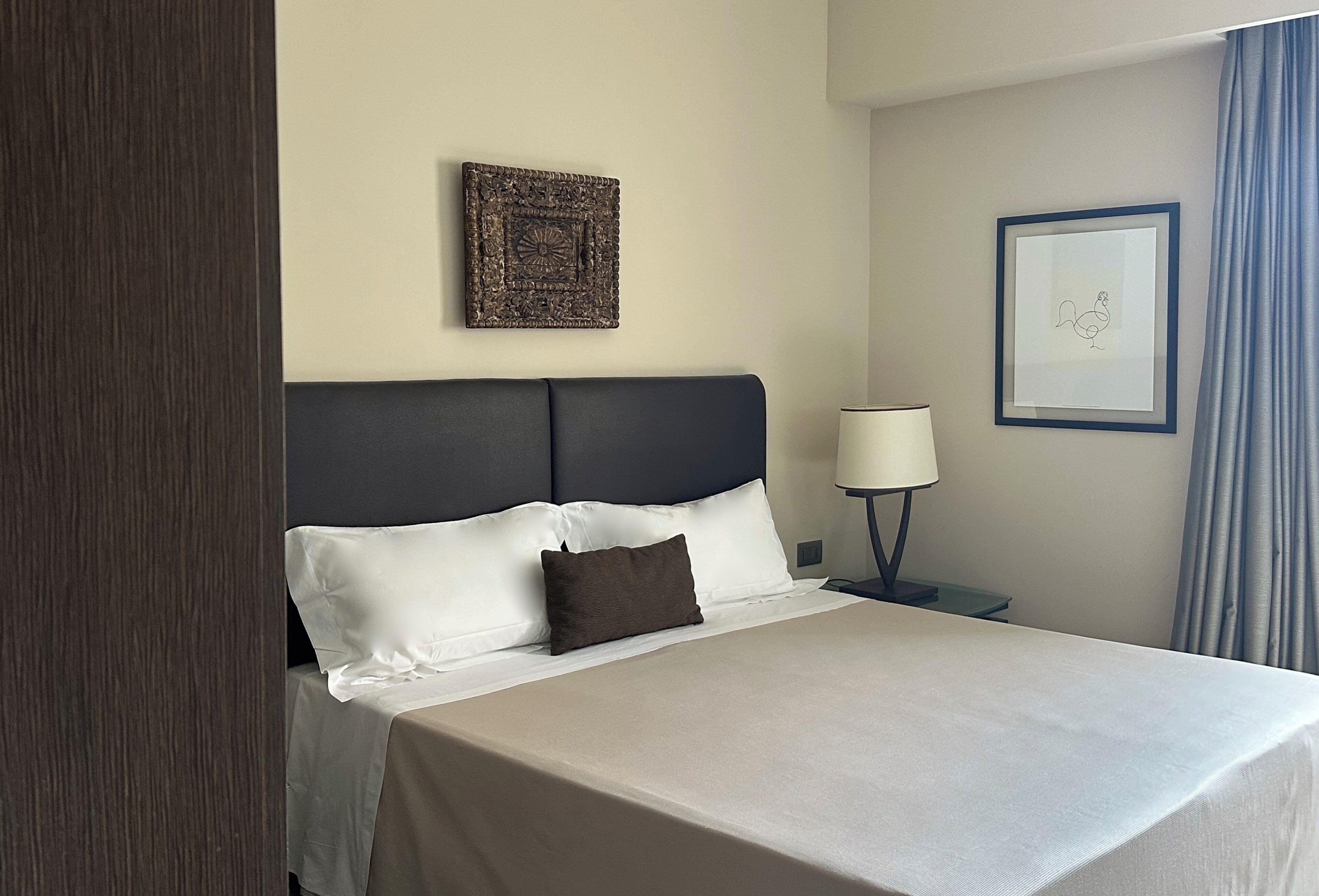 A hotel room with a bed, a nightstand, a lamp, and two framed pictures on the wall.