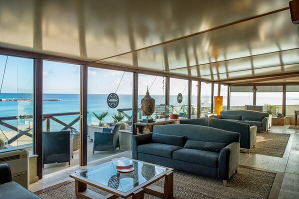 A spacious living area with a large glass wall overlooking the sea, furnished with sofas and a coffee table. - Hotel Capo San Vito (San Vito Lo Capo)