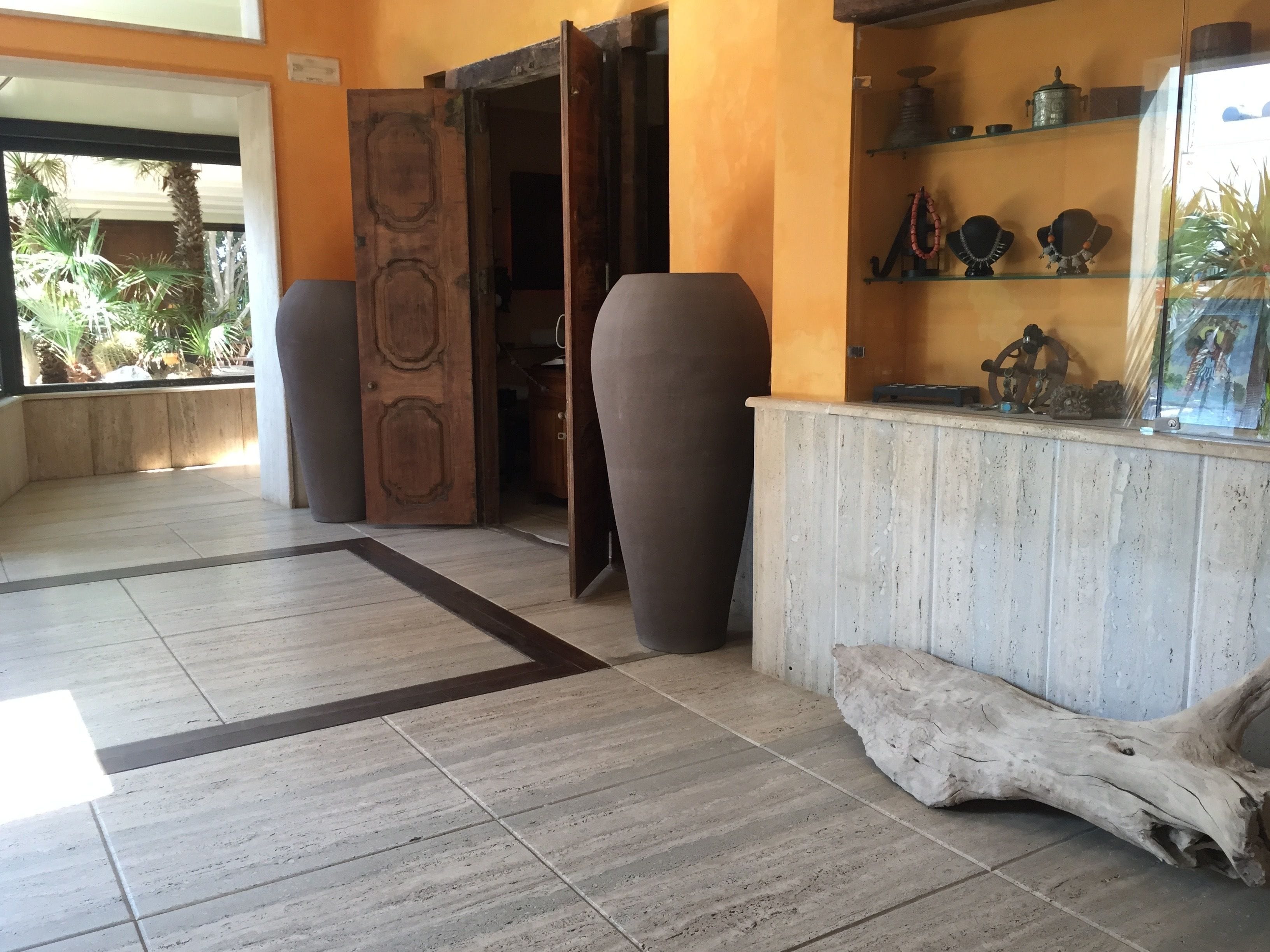 A reception area with a wooden door, a large vase, and a display shelf with decorative items.
