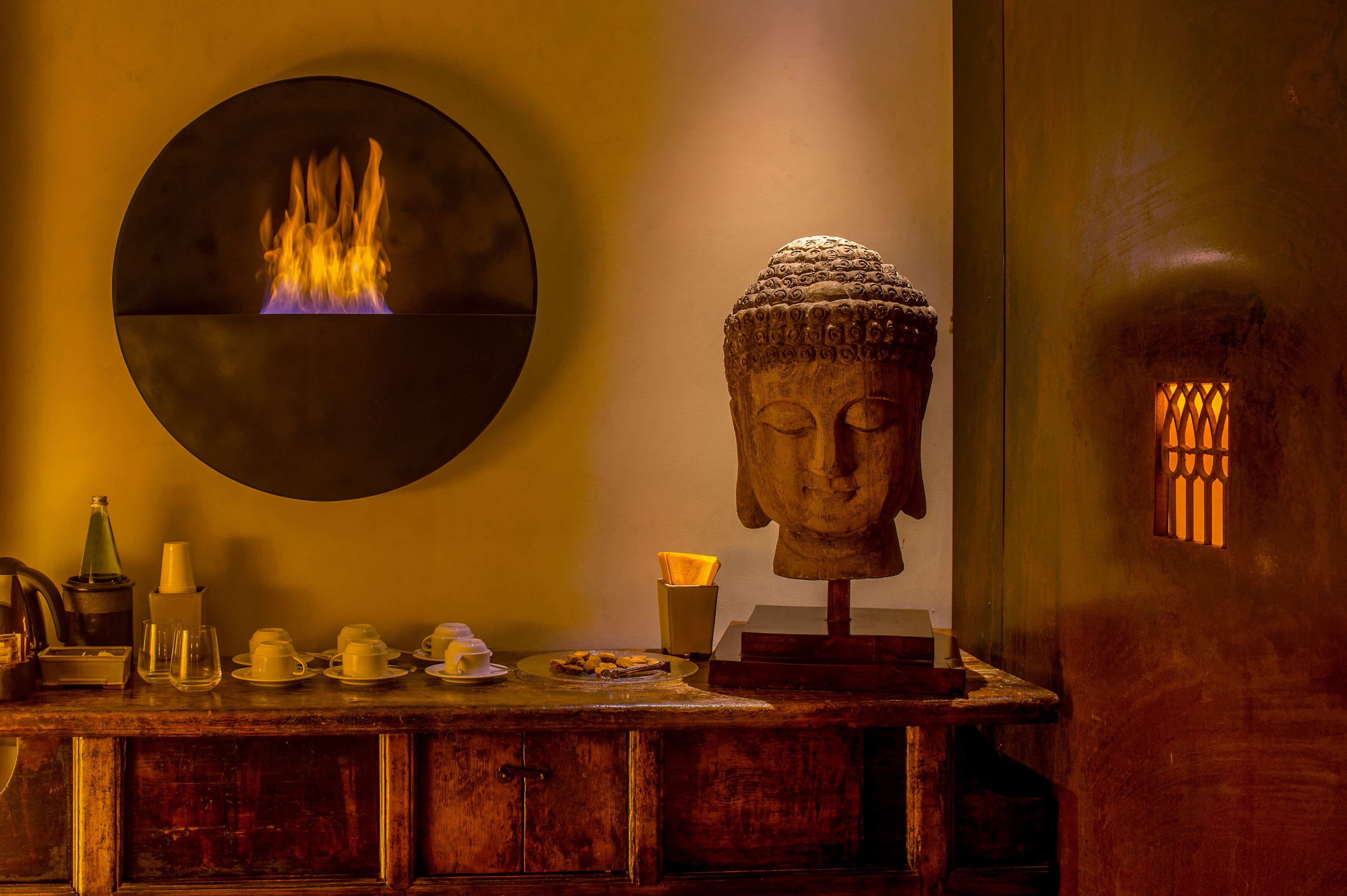 A Buddha statue, a wall-mounted circular screen with a fire, and a wooden counter with tea sets.