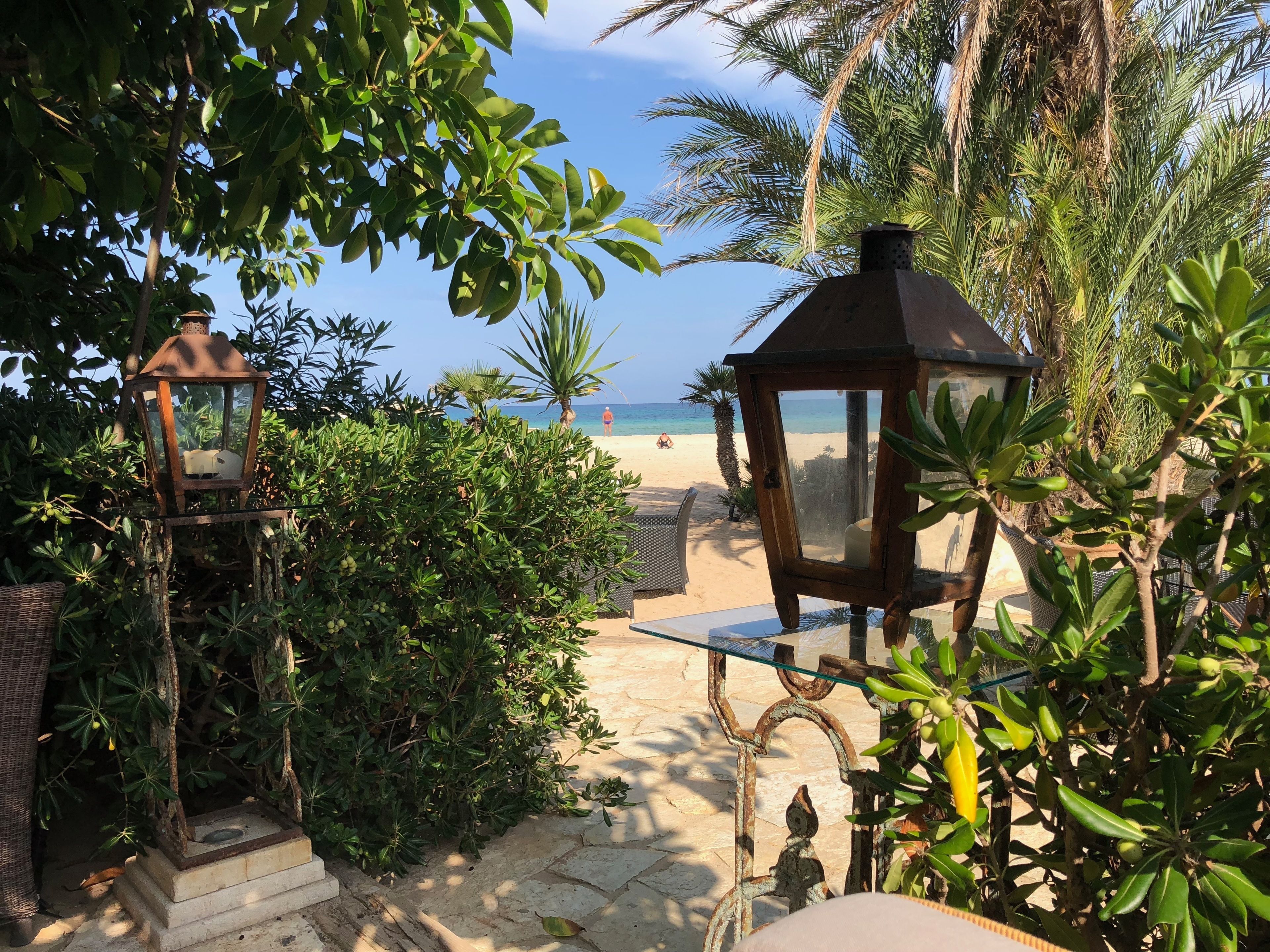 Un sentier menant à une plage, avec une lanterne et une chaise, le tout entouré d’une végétation luxuriante.