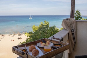 A breakfast tray with croissants, fruit, and orange juice on a balcony overlooking a beach with a clear view of the sea and boats. - Hotel Capo San Vito (San Vito Lo Capo)
