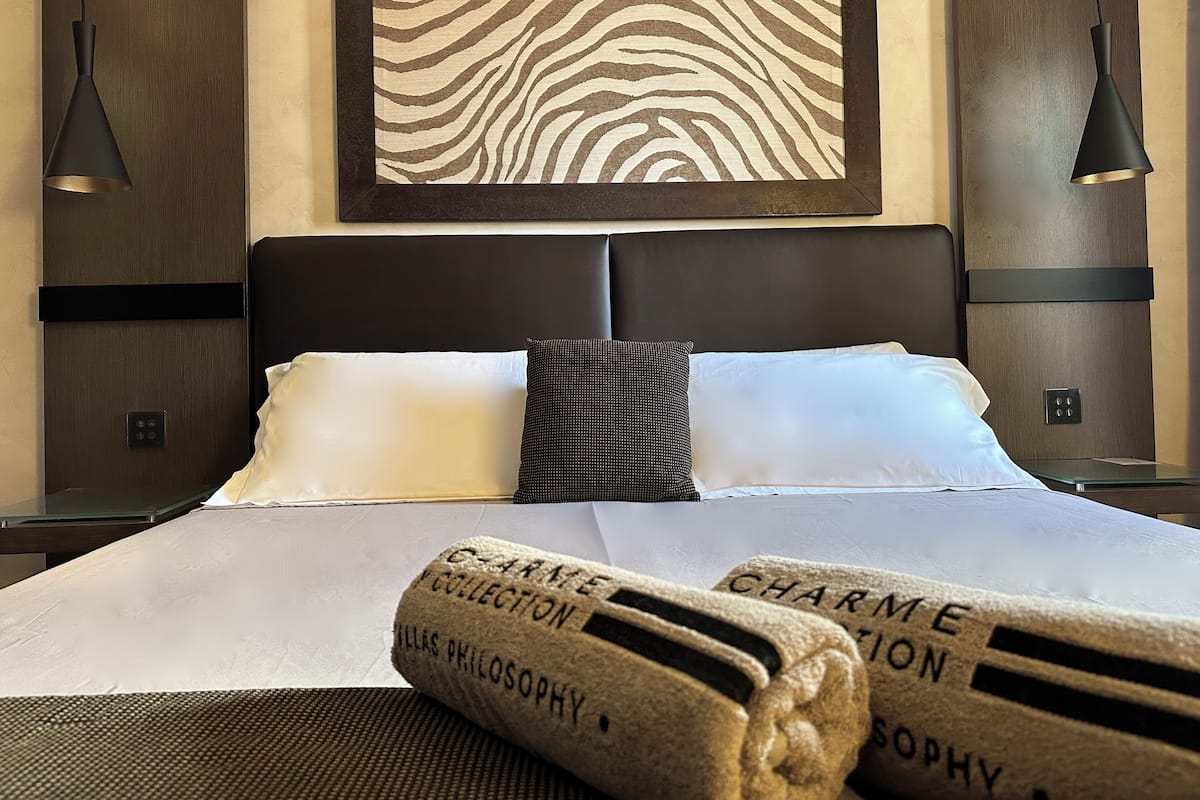 A hotel room with a large bed, two bedside tables, a zebra-patterned artwork, and two pendant lights.