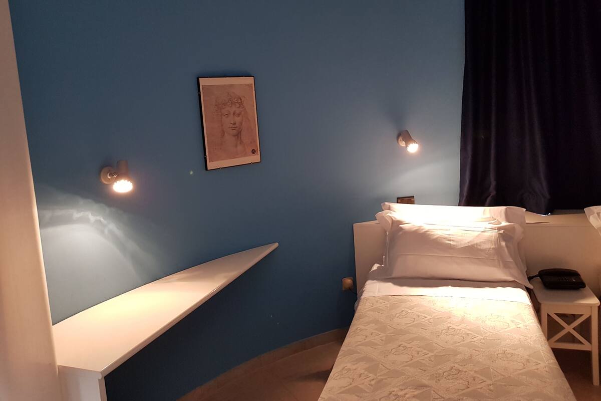 A bedroom with a bed, bedside table, and a wall-mounted light fixture.