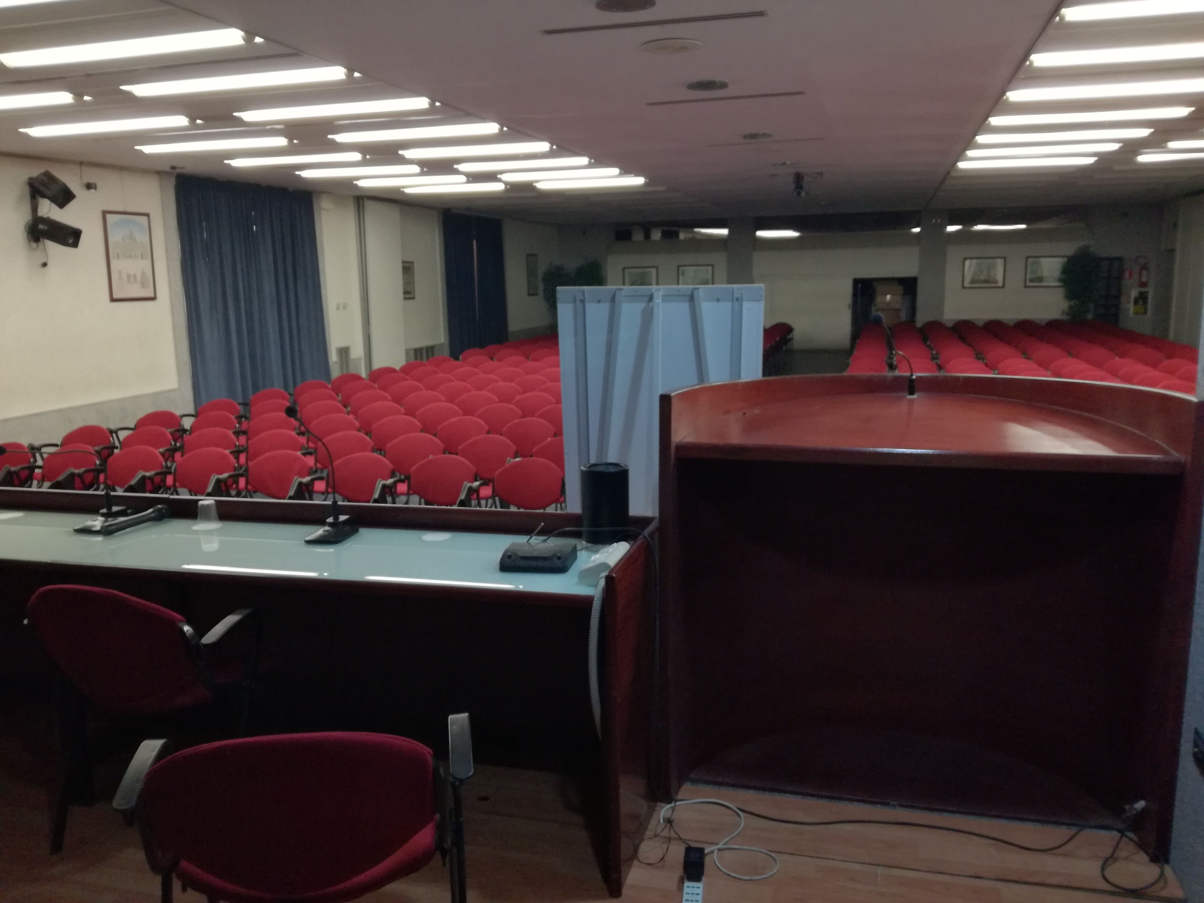 A conference room with rows of red chairs, a podium, and a presentation screen.