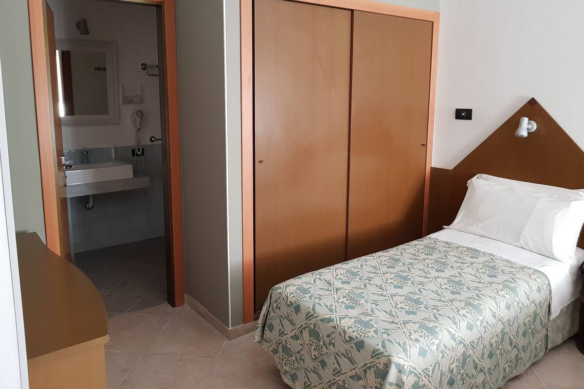 A bedroom with a bed, a wardrobe, and a bathroom visible through an open door.