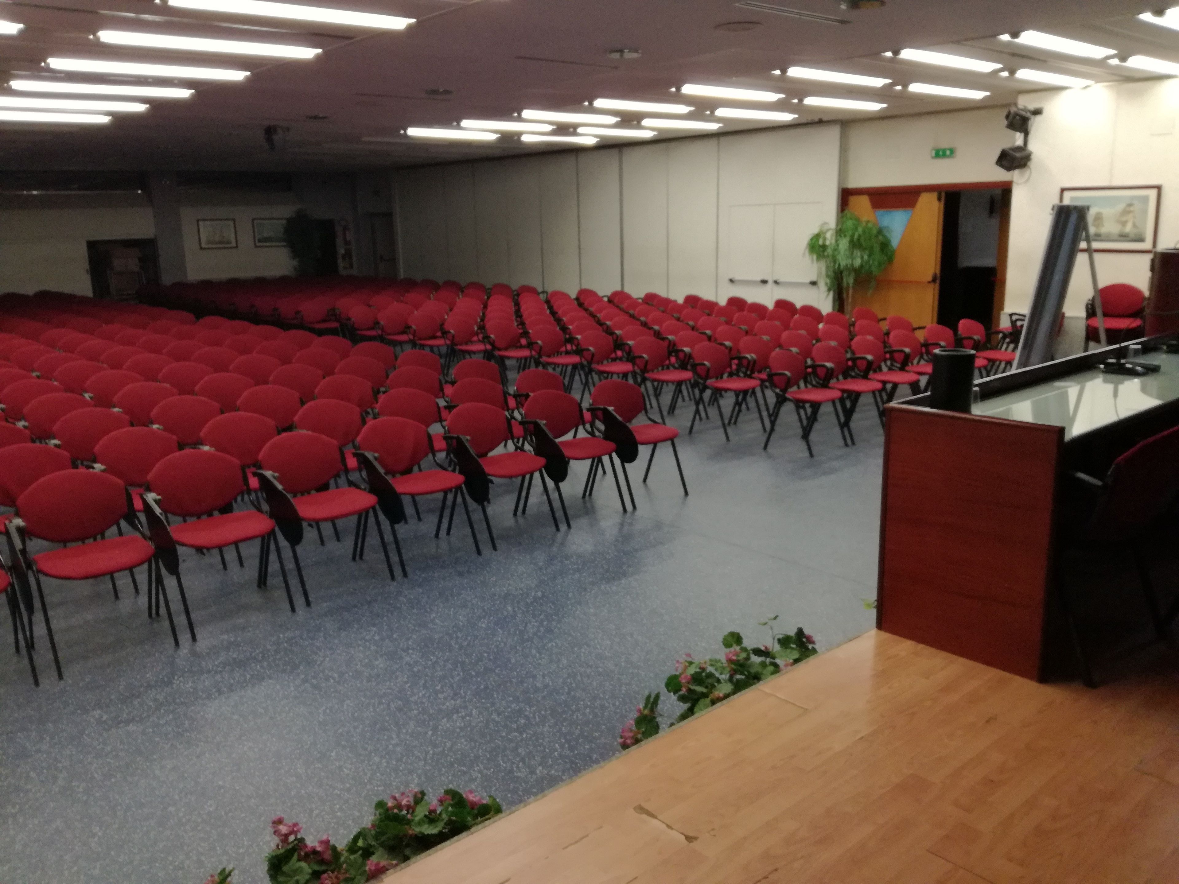 A conference room with rows of red chairs and a podium at the front.