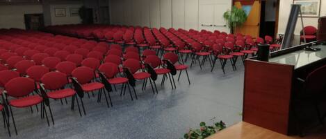 A conference room with rows of red chairs and a podium at the front.