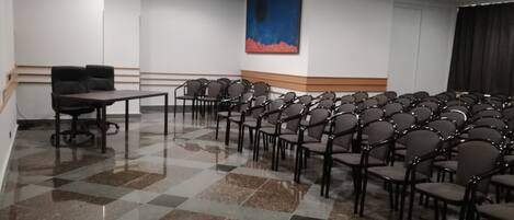 A conference room with a checkered floor, rows of chairs, a table, and a projector on the ceiling.