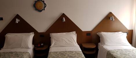 Habitación de hotel con tres camas individuales, cada una con una colcha estampada, una mesita de noche pequeña y una lámpara de pared.