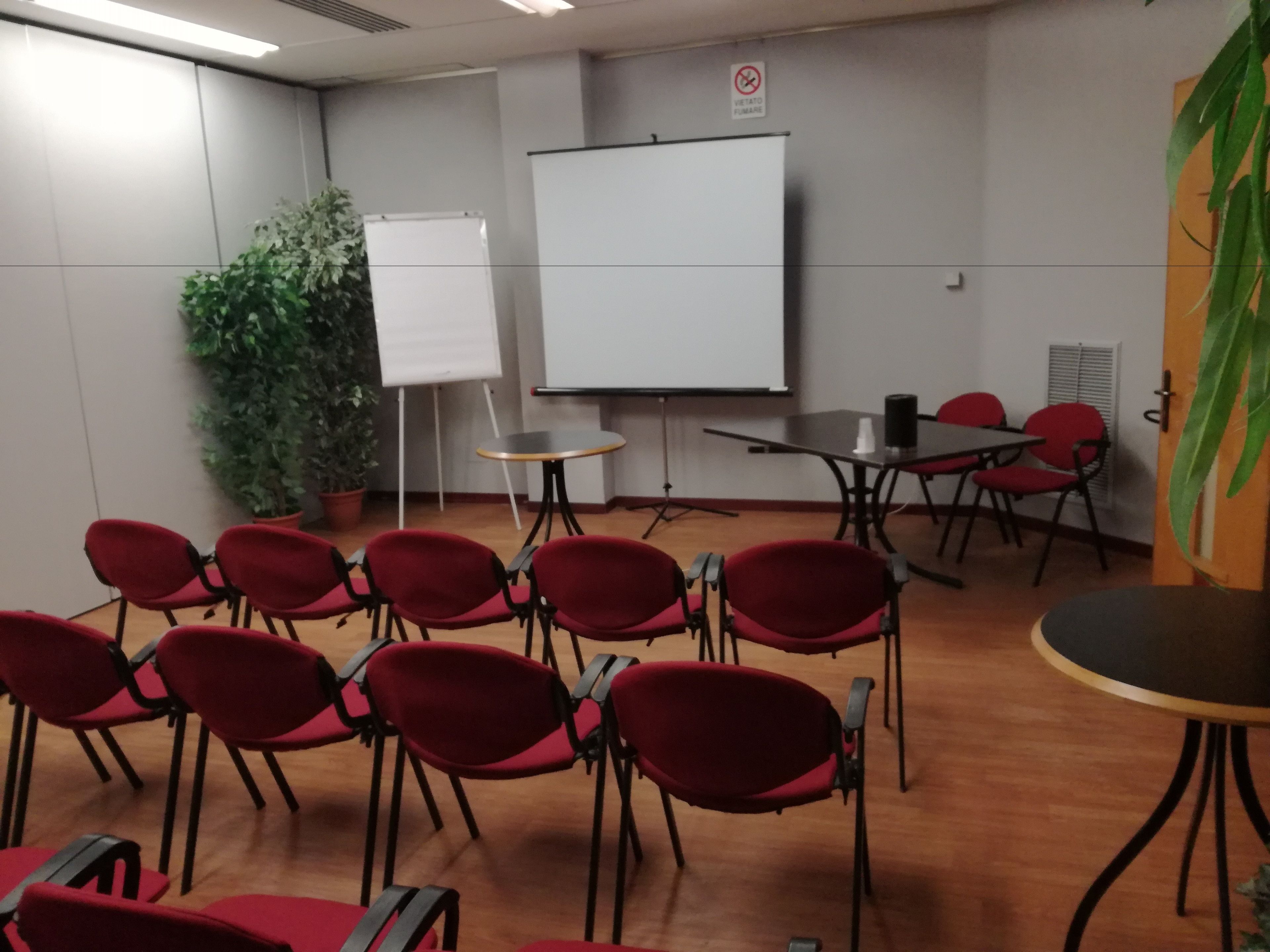 A conference room with red chairs, a whiteboard, a projector screen, and a potted plant.