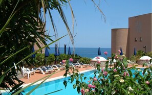 A poolside area with lounge chairs and umbrellas, a clear view of the ocean, and a building in the background.