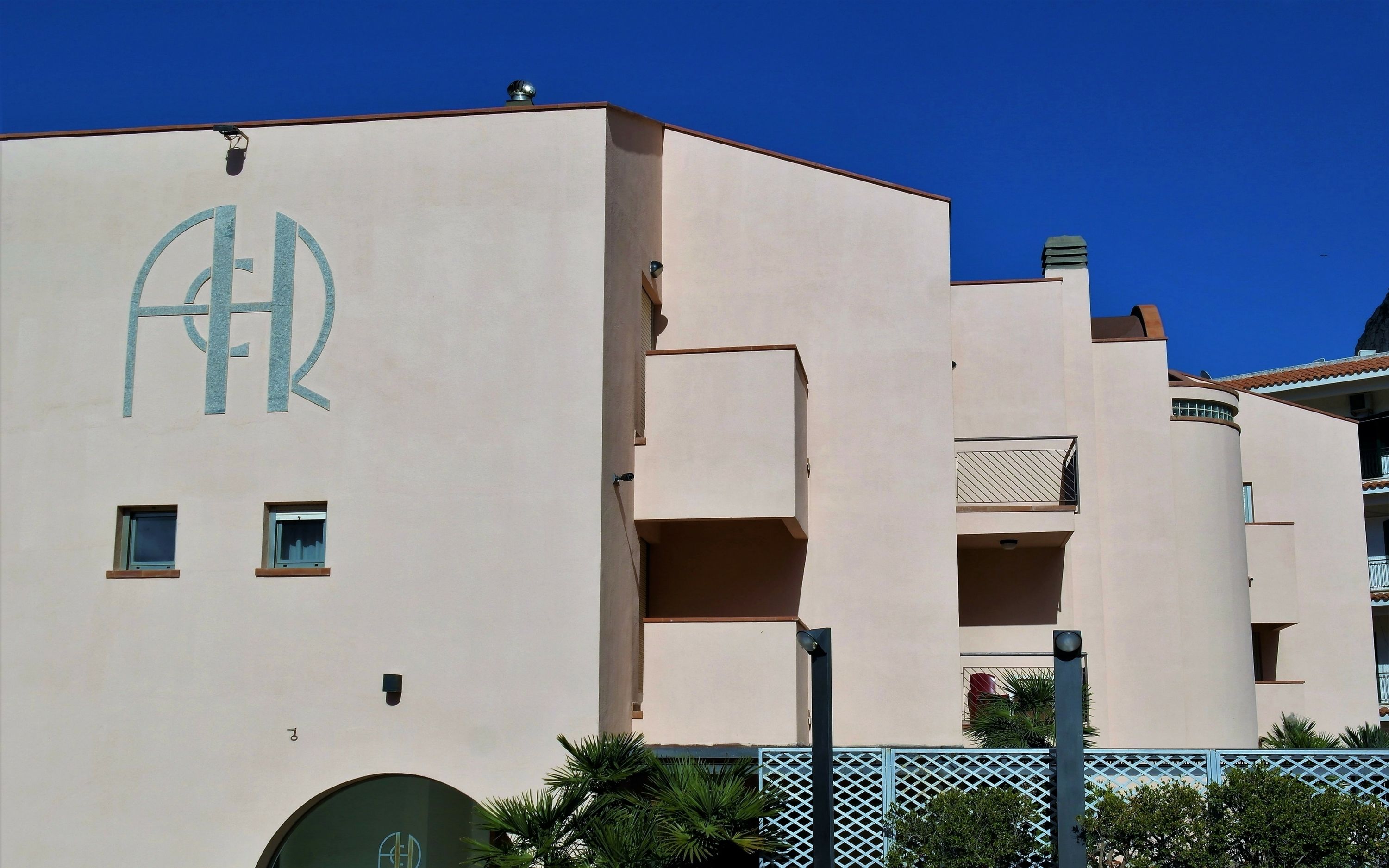 A building with a large 'A' and 'R' logo, multiple balconies, and a gated entrance.