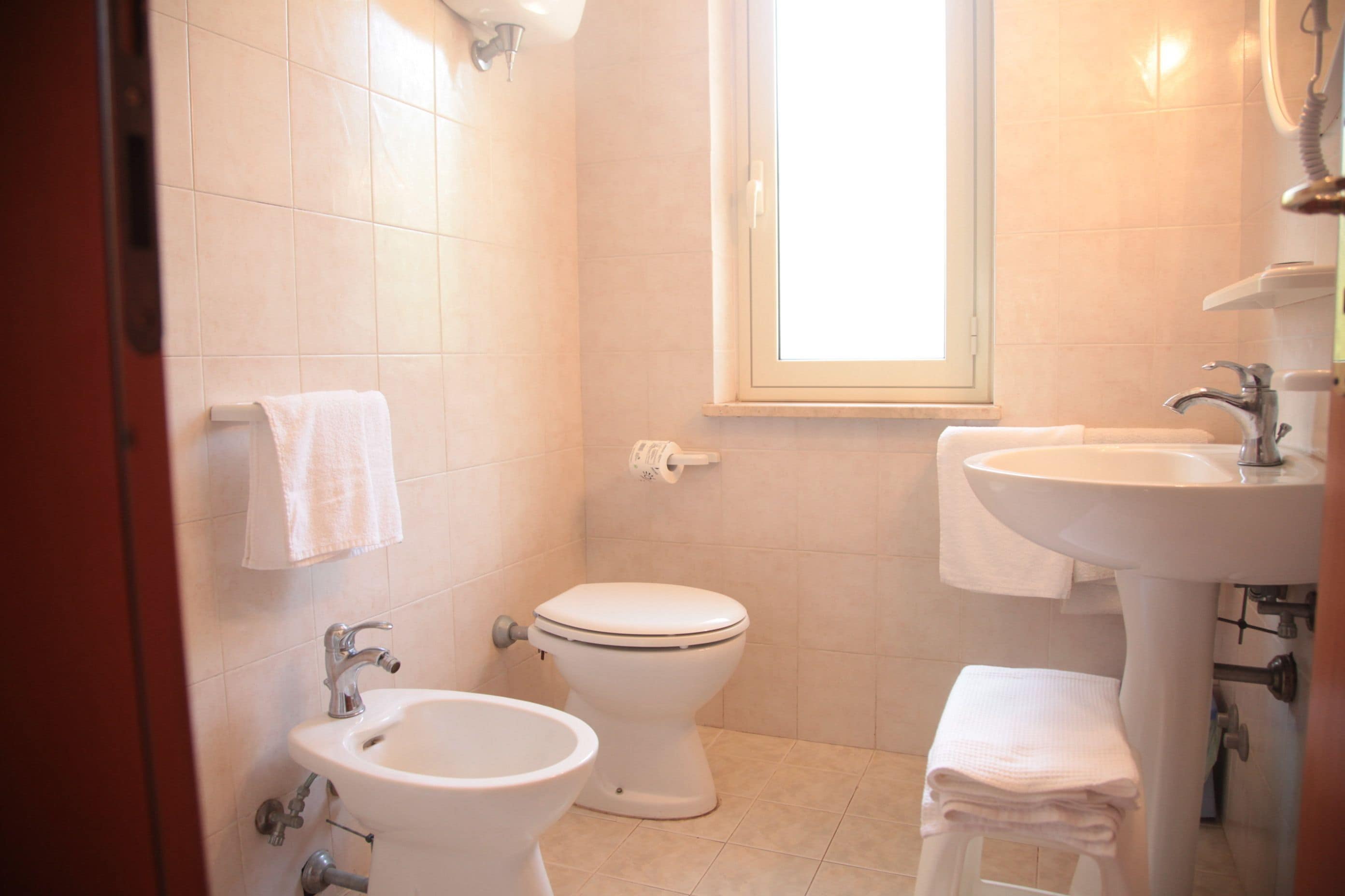 Une salle de bain comprenant des toilettes, un bidet, un lavabo et une fenêtre.