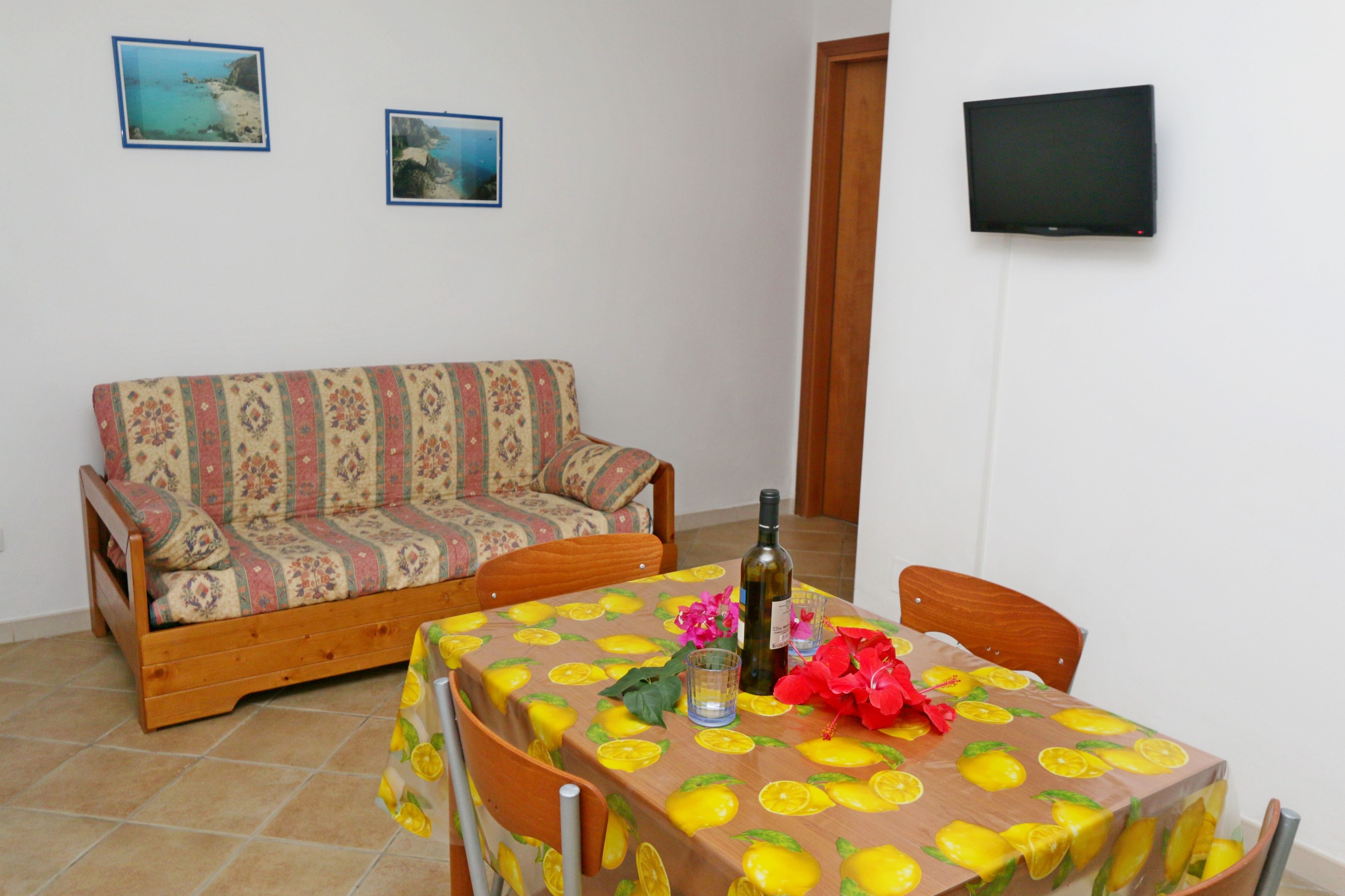 A room with a sofa, a dining table with a lemon pattern, a bottle, and a flower.