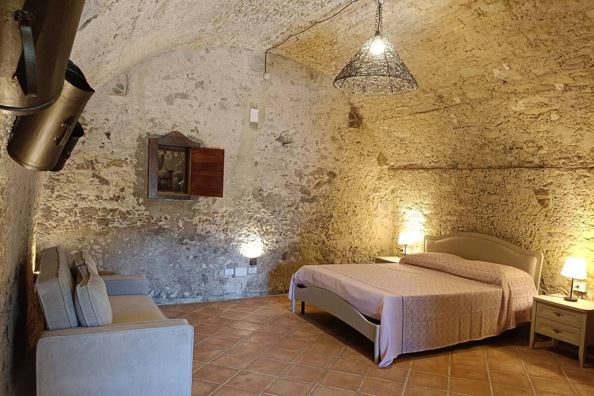A rustic room with a bed, bedside lamps, a chair, and a hanging light fixture.