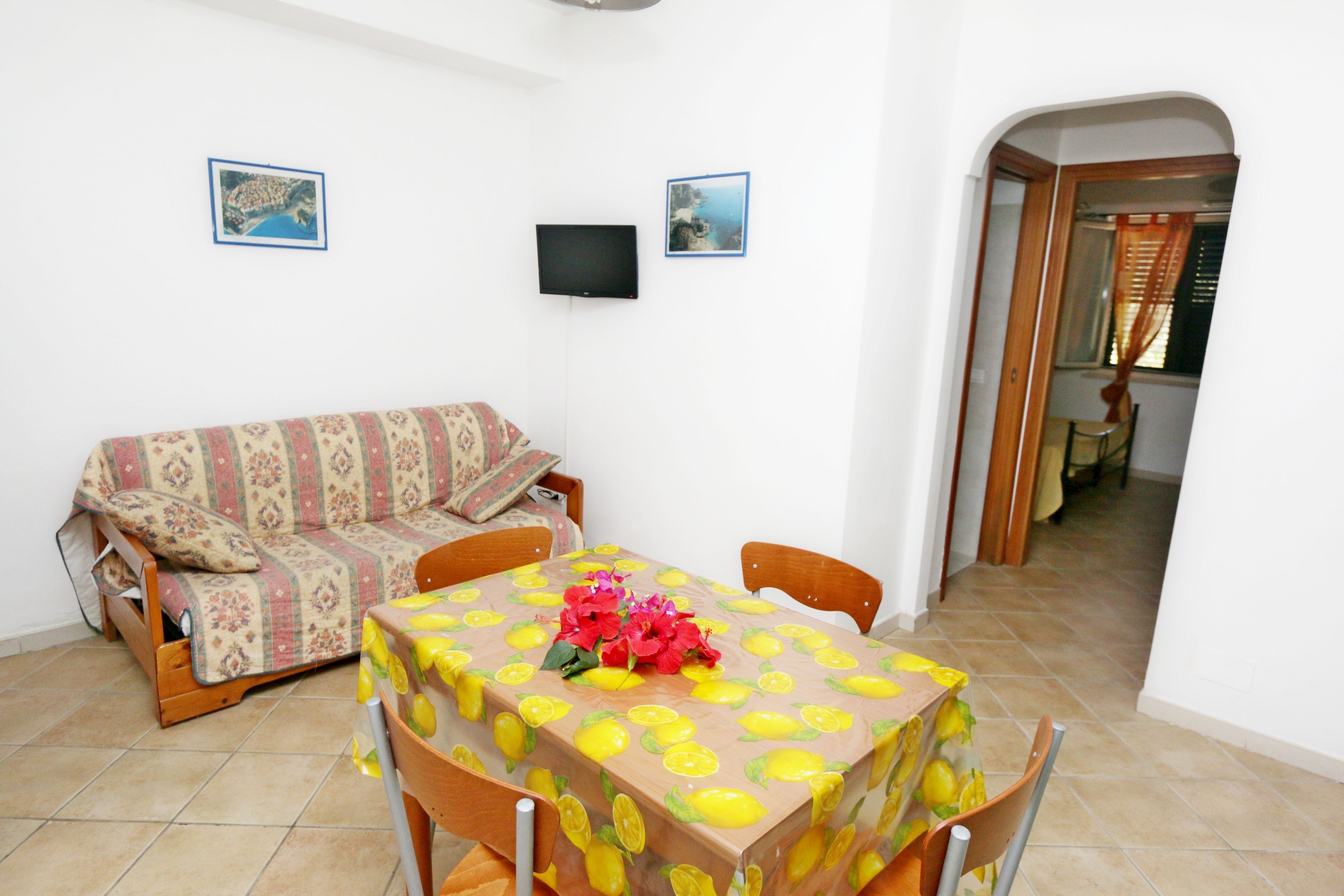 A small, furnished room with a sofa, a table with a lemon pattern, and two framed pictures on the wall.