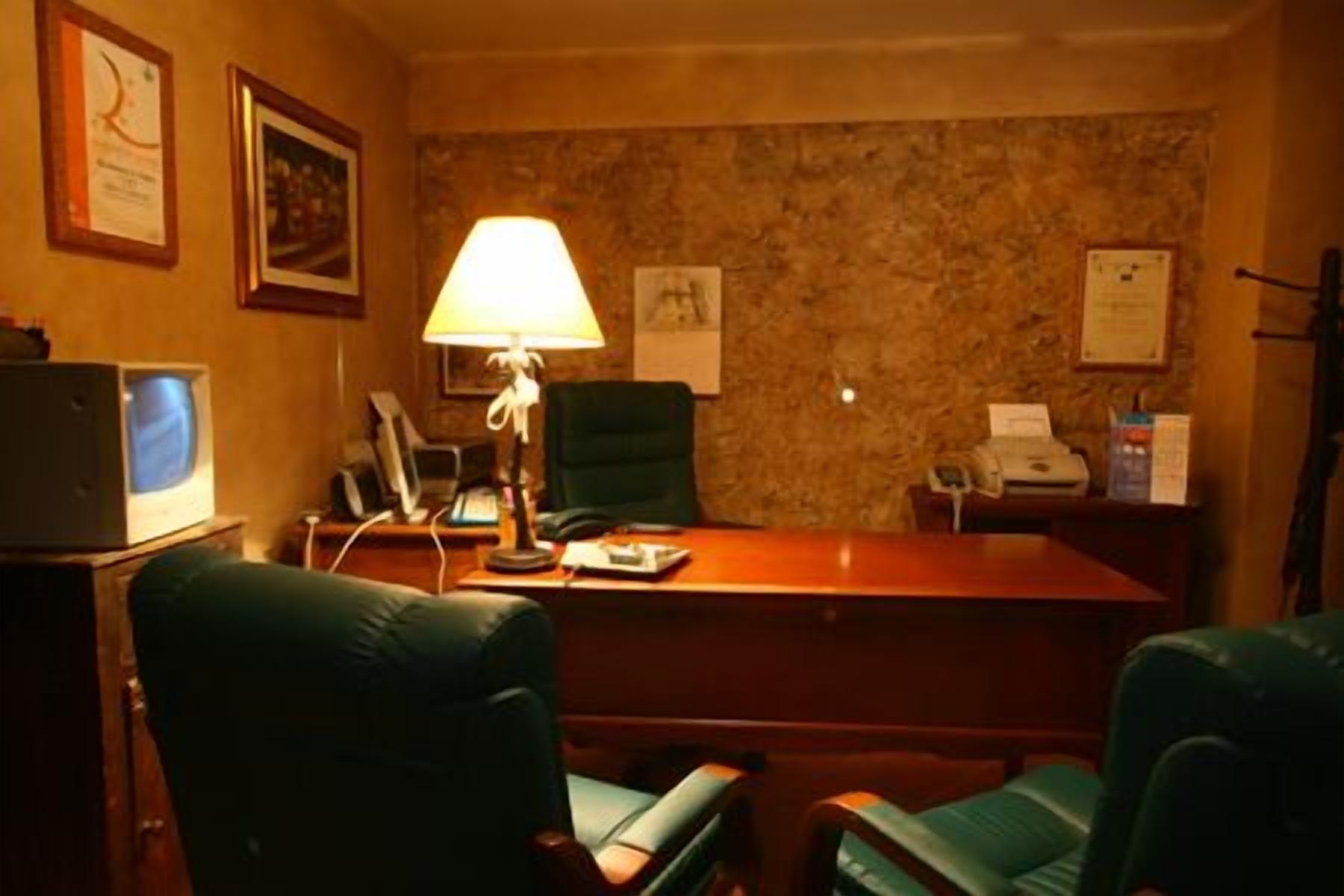 A conference room with a wooden table, two green chairs, a desk lamp, a telephone, and framed certificates on the wall.