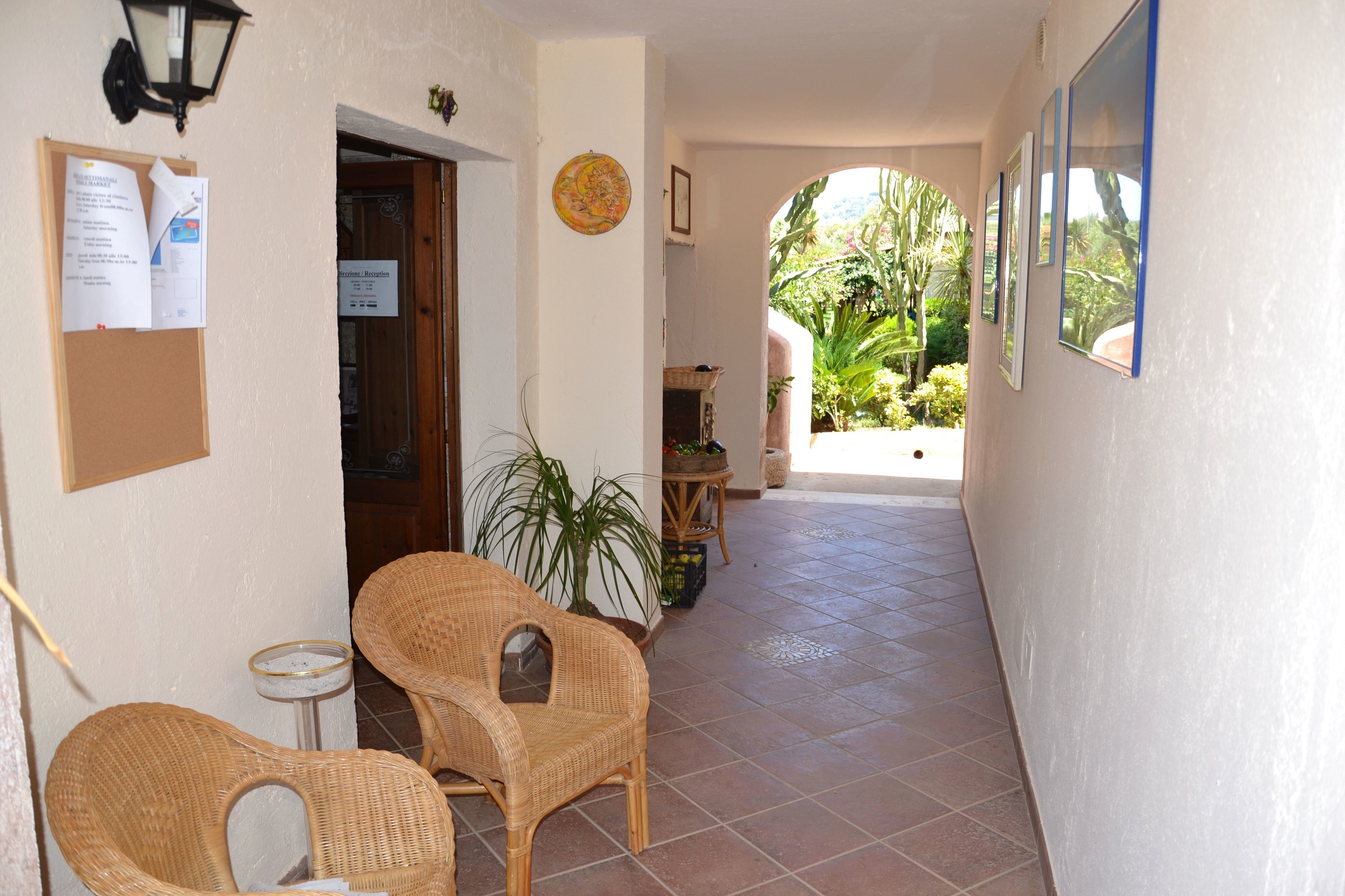A corridor with wicker chairs, a bulletin board, and a view of a garden.