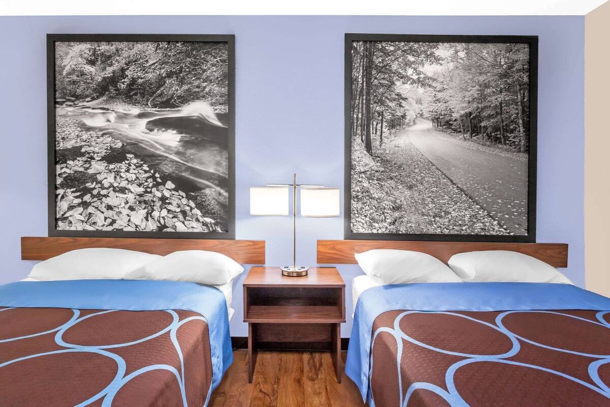 Une chambre d’hôtel avec deux lits, une table de chevet, une lampe et deux grandes photographies en noir et blanc accrochées au mur.