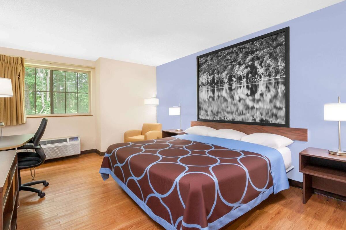 Une chambre d’hôtel avec un lit, un bureau, des chaises et une grande fenêtre.