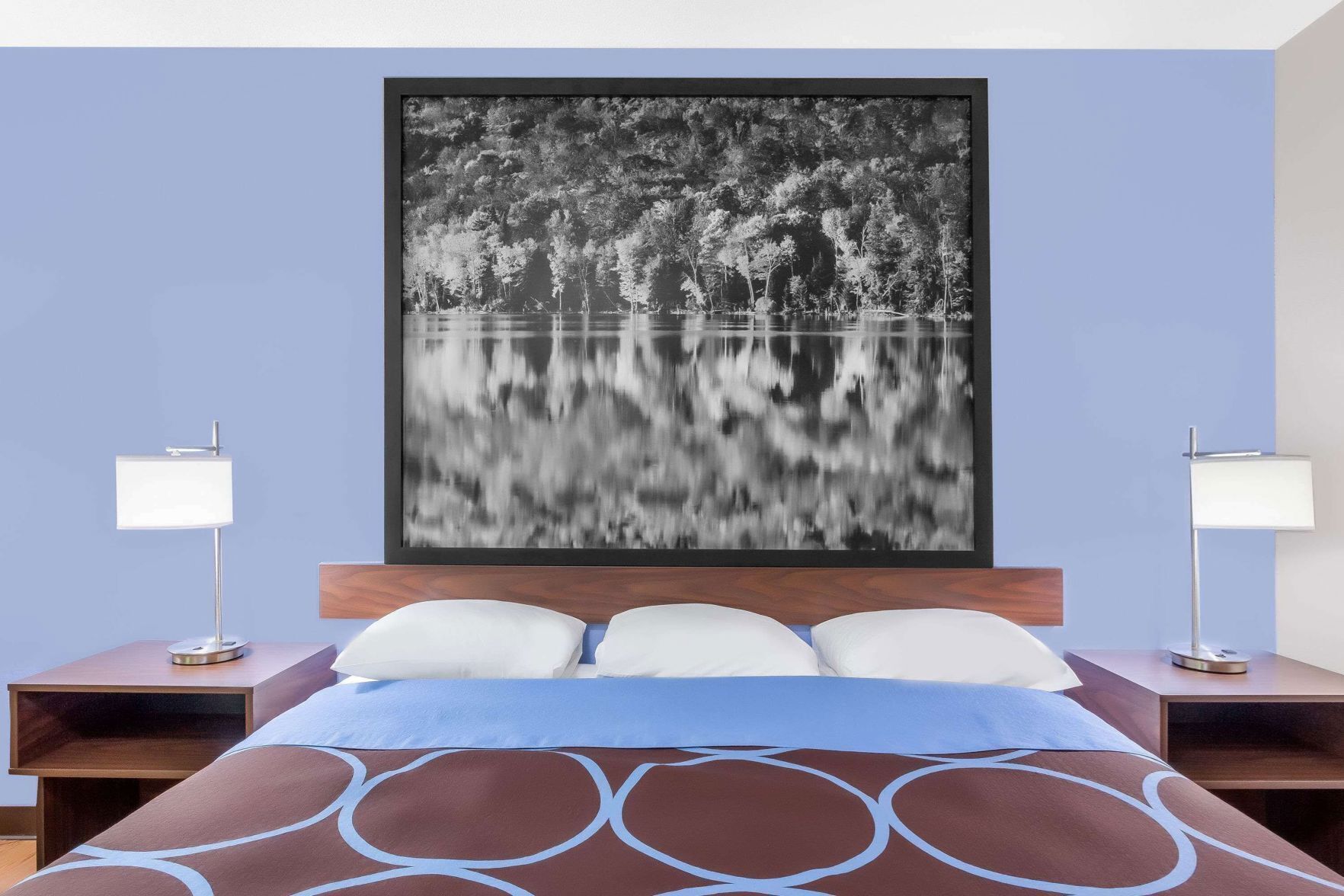 Una habitación de hotel con una cama, dos mesitas de noche y un cuadro grande en la pared.