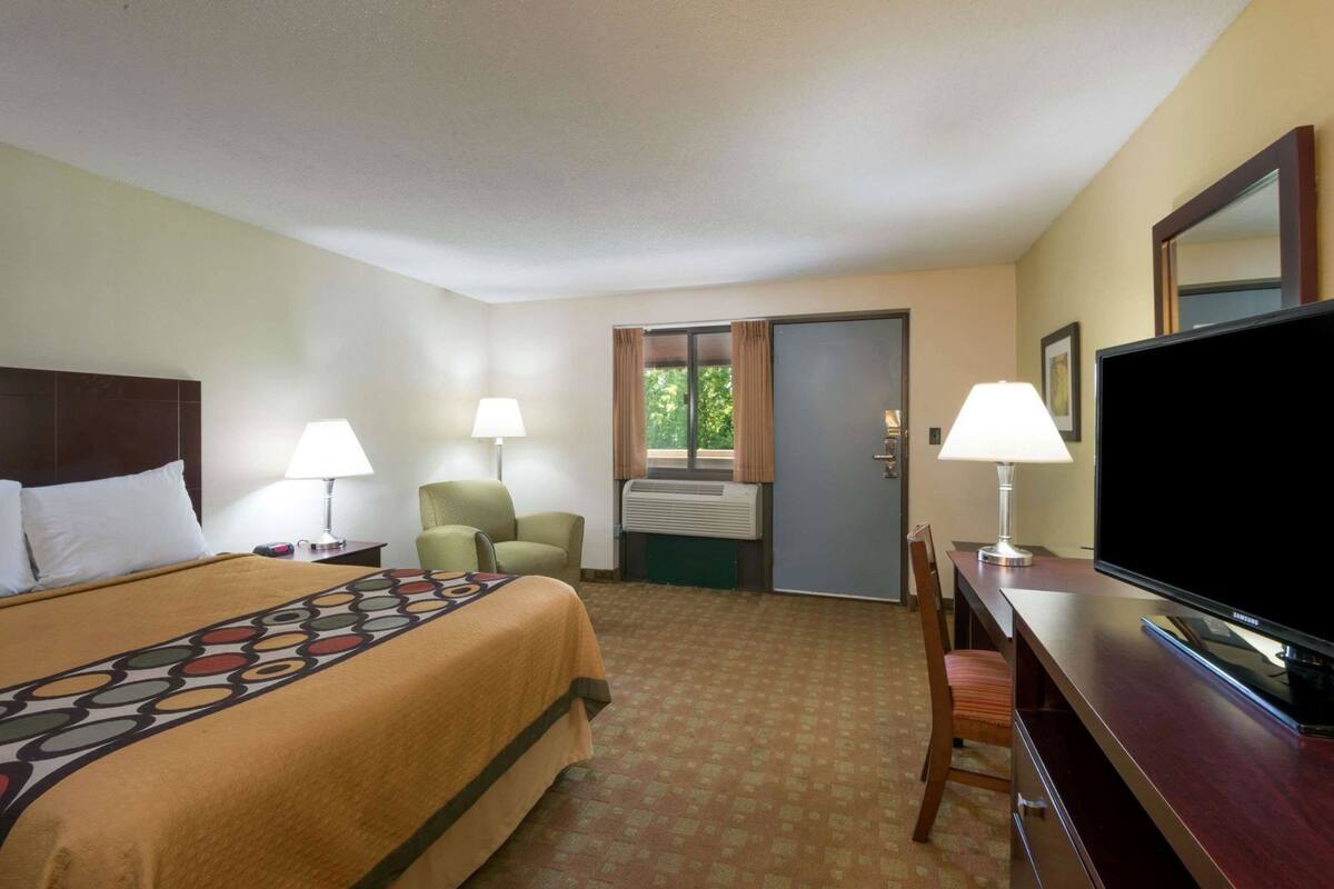 Une chambre d’hôtel comprenant un lit, deux chaises, un bureau avec une télévision et une porte donnant sur un balcon.