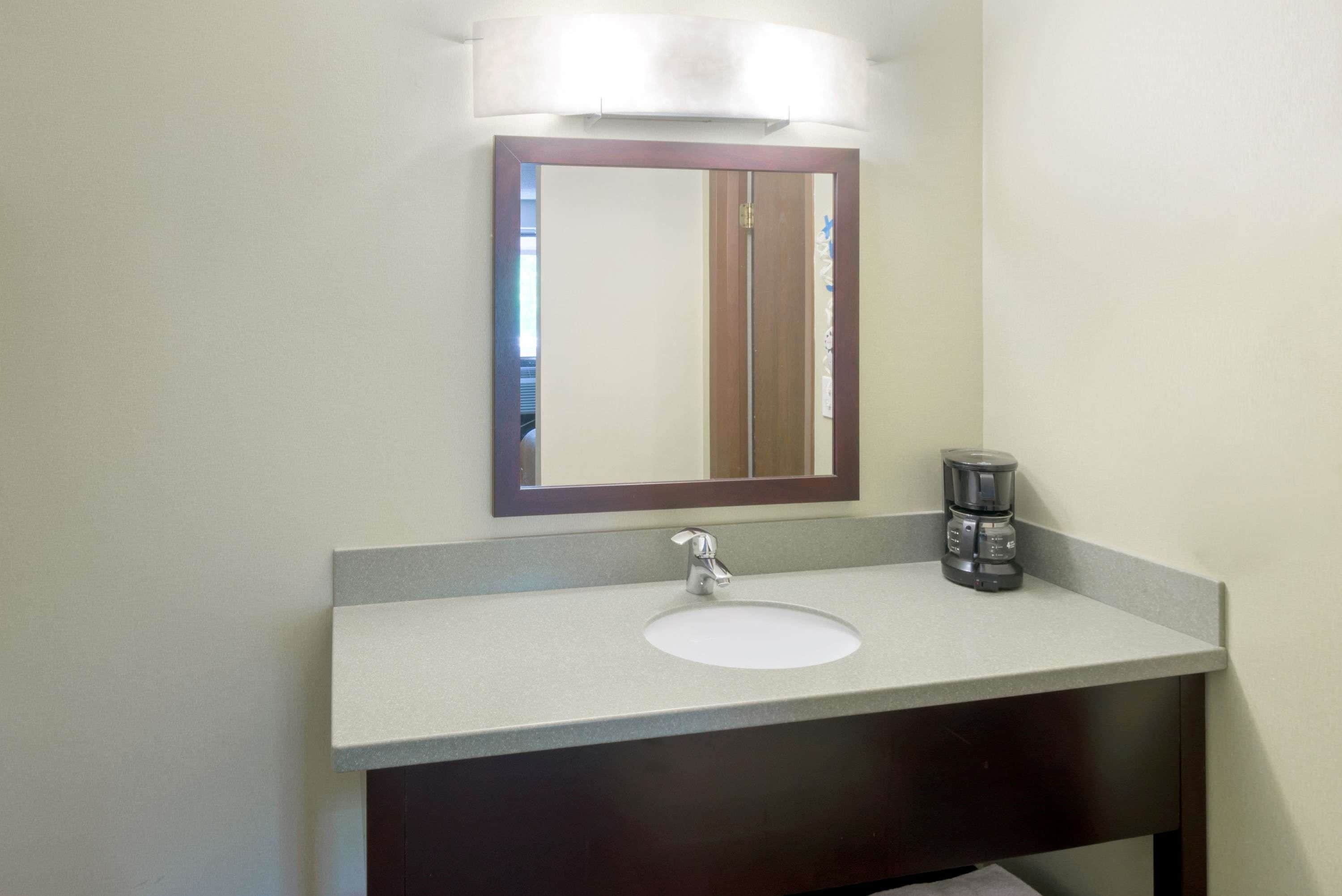 A bathroom with a white sink, a dark vanity, a mirror with a wooden frame, and a coffee maker on the counter.