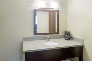 Un baño con un lavamanos blanco, un mueble de tocador oscuro, un espejo con marco de madera y una cafetera sobre la encimera.