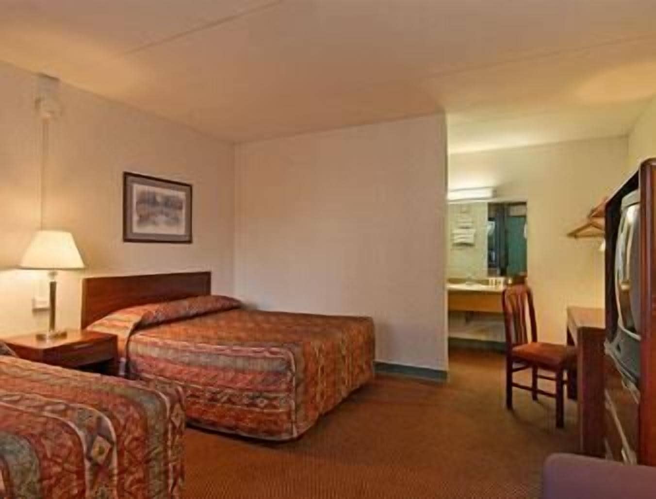 Une chambre d’hôtel avec deux lits, un bureau, une chaise et un téléviseur.