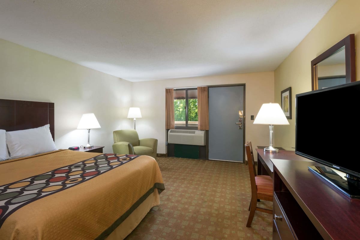 Une chambre d’hôtel comprenant un lit, deux chaises, un bureau avec une télévision et une porte donnant sur un balcon.