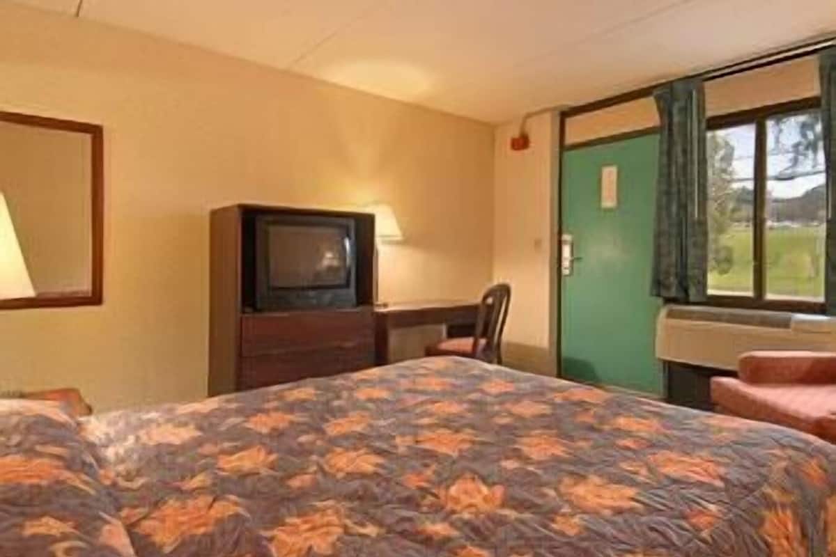 Une chambre avec un lit, un bureau, une télévision et une fenêtre avec des rideaux.
