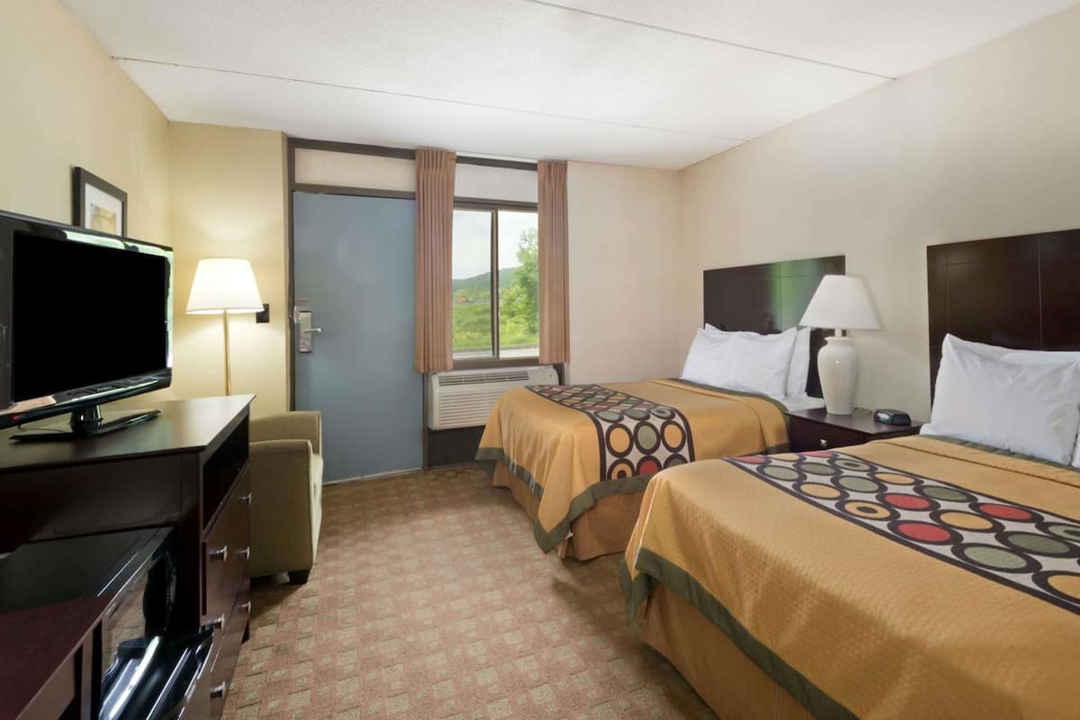 Une chambre d’hôtel avec deux lits, une télévision, un bureau et une fenêtre avec des rideaux.