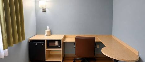 A small room with a desk, a chair, a microwave, and a small cabinet.