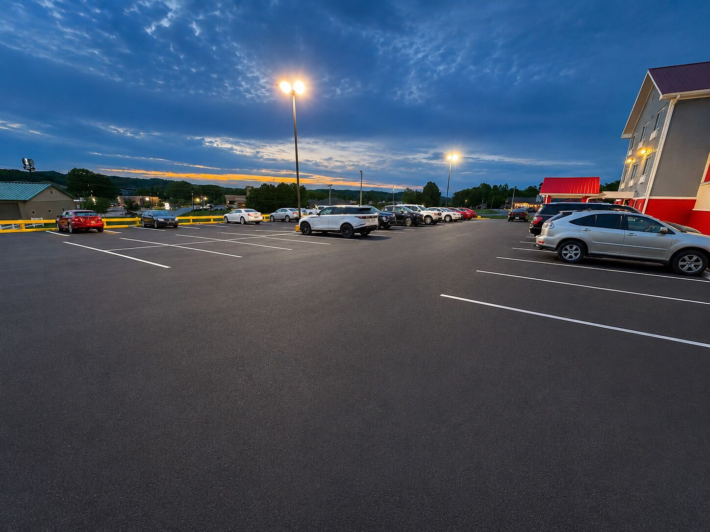 A parking lot with multiple cars, a building with a red roof, and street lamps.