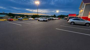 A parking lot with multiple cars, a building with a red roof, and street lamps.