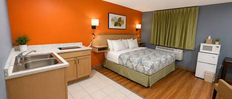 A hotel room with a bed, a small kitchenette, a sink, and a microwave.