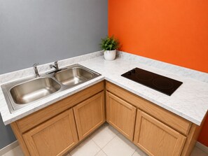 A kitchen with a double sink, a black induction cooktop, wooden cabinets, and a potted plant. - Motel 6 Morehead, KY (Morehead)