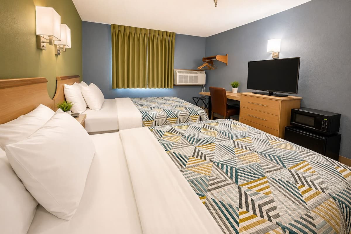 A hotel room with two beds, a desk, a TV, and a microwave.