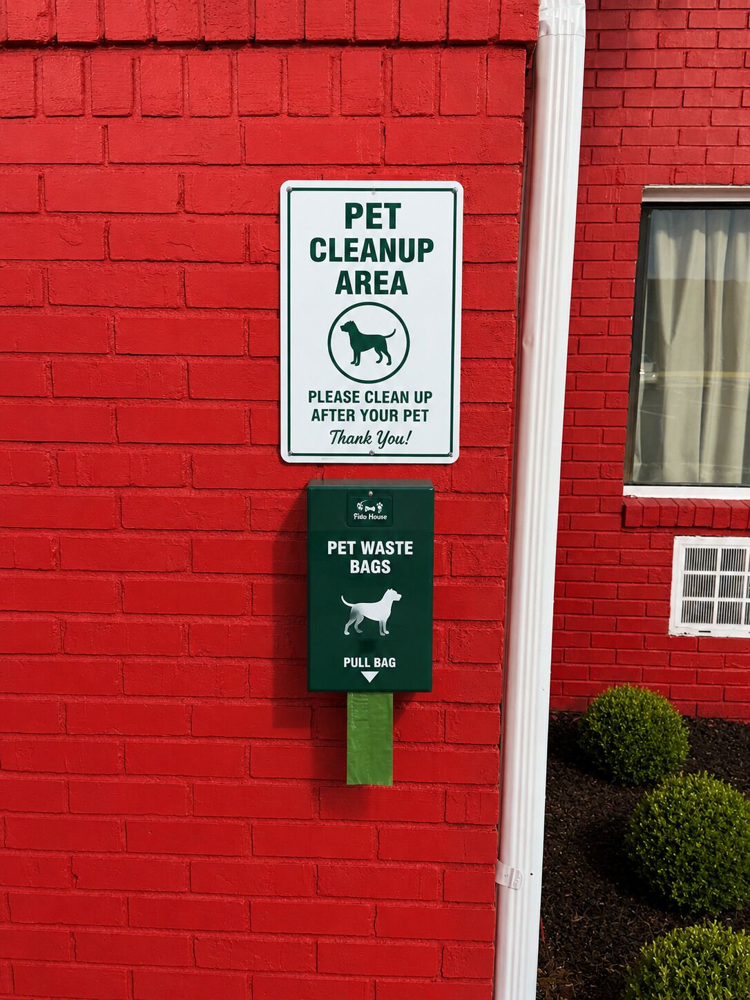A red brick wall with a pet cleanup area sign and a pet waste bag dispenser.